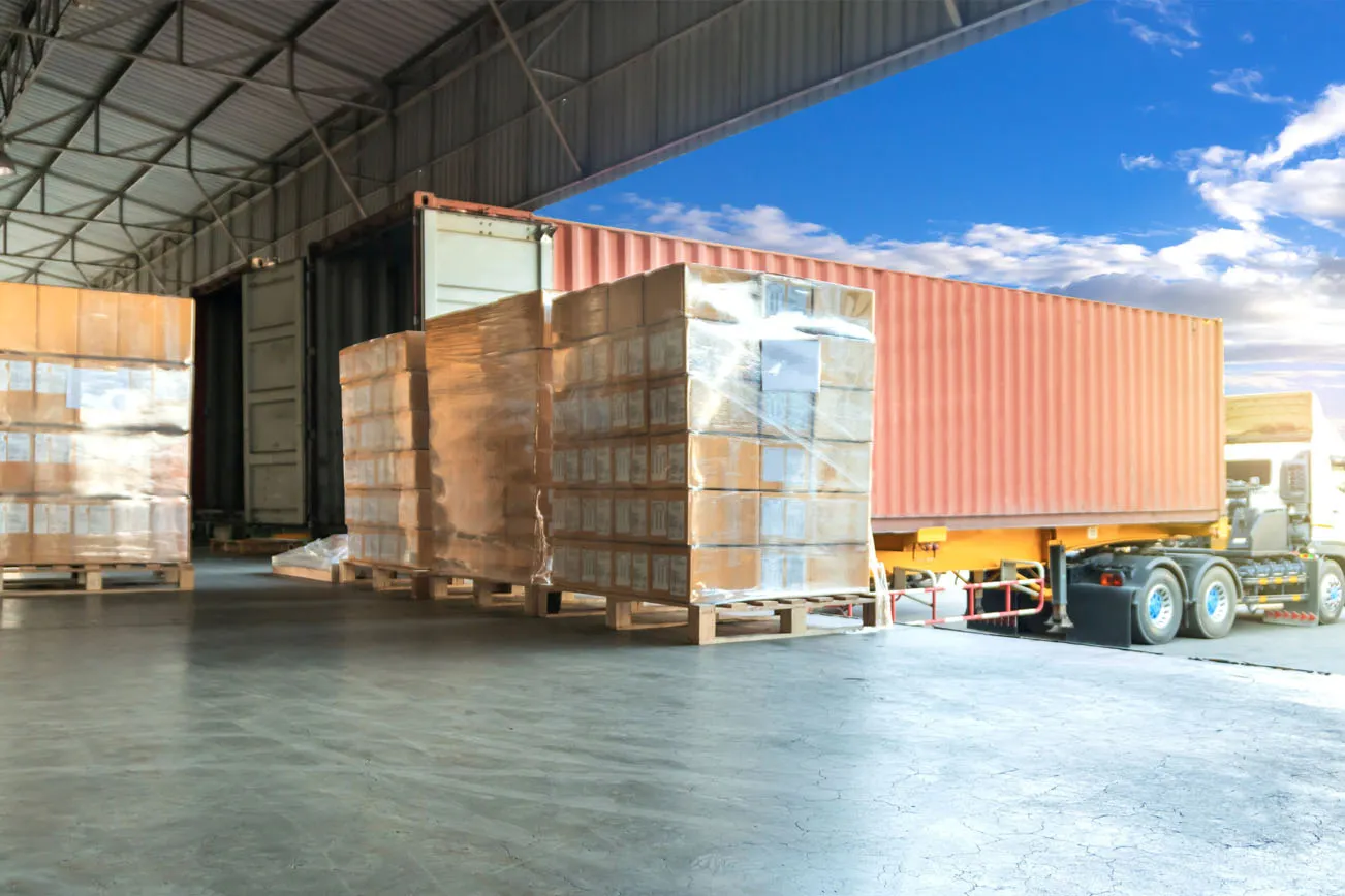 Shrink-wrapped pallets staged at a loading dock beside a shipping container